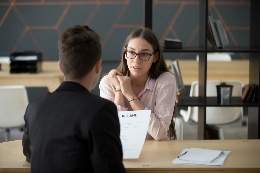 Confident millennial female applicant talking at job interview answering questions, young serious candidate speaking to hr telling about work experience, introduction and first impression concept