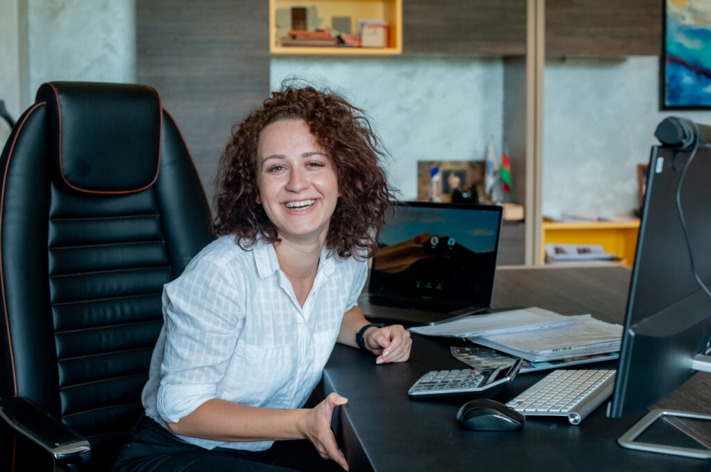 portrait of young office worker woman sitting at office desk using laptop computer looking at camera smiling cheerfully working in bright office.