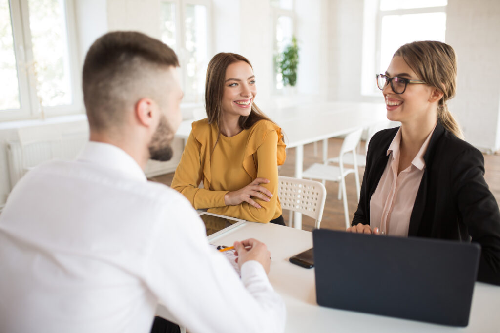 Two cheerful business women happily talking with male applicant for work. Young smiling employers spending job interview in modern office